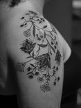 Tatuagem ornamental feita em linha fina (fineline), na região do ombro e braço, somente em preto (blackwork), representando ornamentos e flores mandalas.