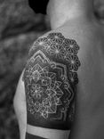 Tatuagem feita em pontilhismo (dotwork) na região do ombro e braço, representando uma flor/mandala e padrões geométricos.