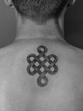 Tatuagem minimalista feita pontilhismo (dorwork) na região da costas, próximo ao pescoço, representando o simbolo budista "nó infinito".
