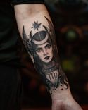 Tatuagem detalhada de uma figura feminina mística, adornada com um crescente lunar e asas laterais. Acima, uma estrela guia; abaixo, o símbolo de Virgem. O olhar profundo e os traços marcantes evocam espiritualidade, poder e conexão cósmica.