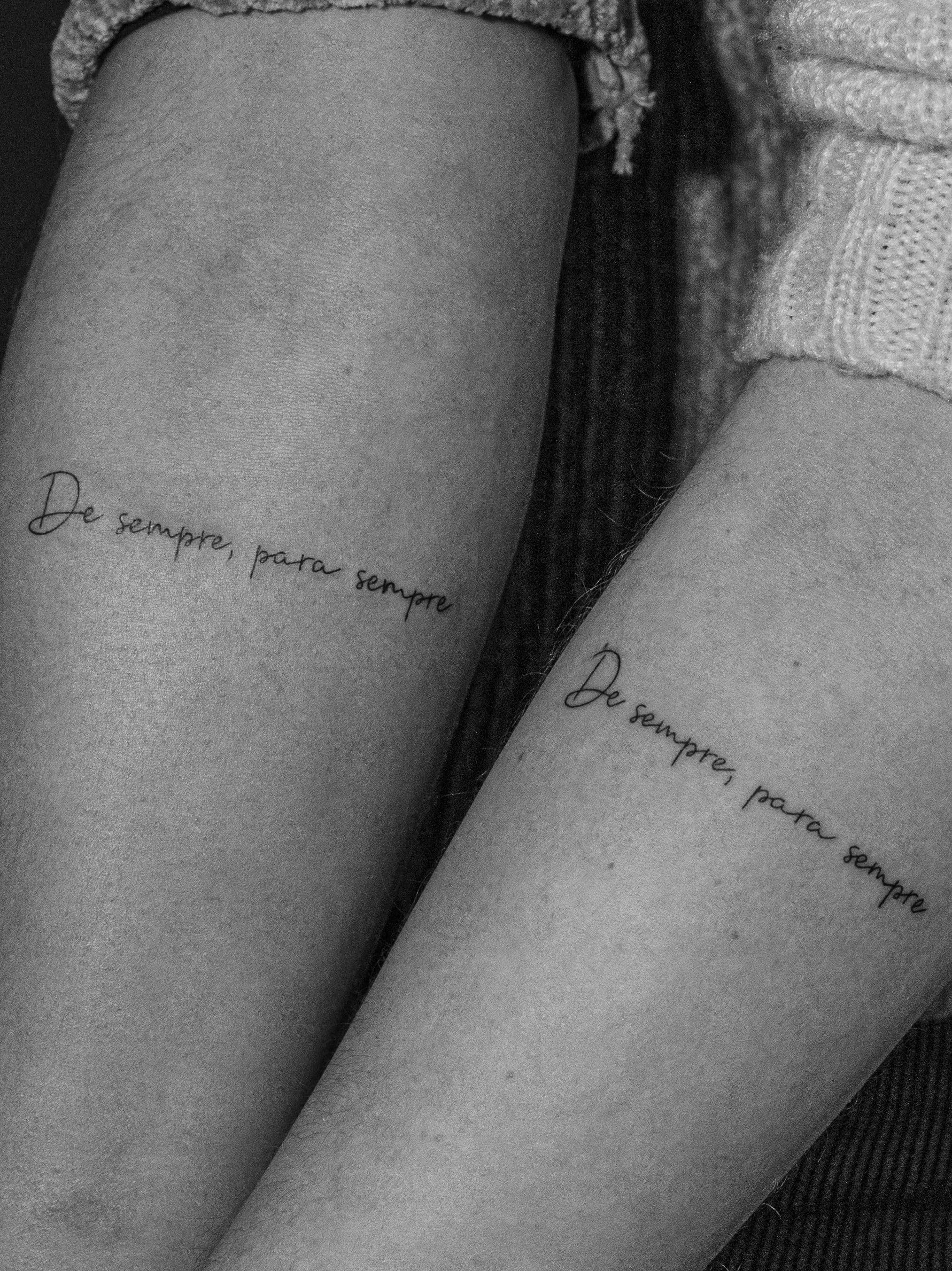 Tatuagem minimalista feita em linha fina (fineline) na região do antebraço, em duas amigas, com a frase "de sempre, para sempre".