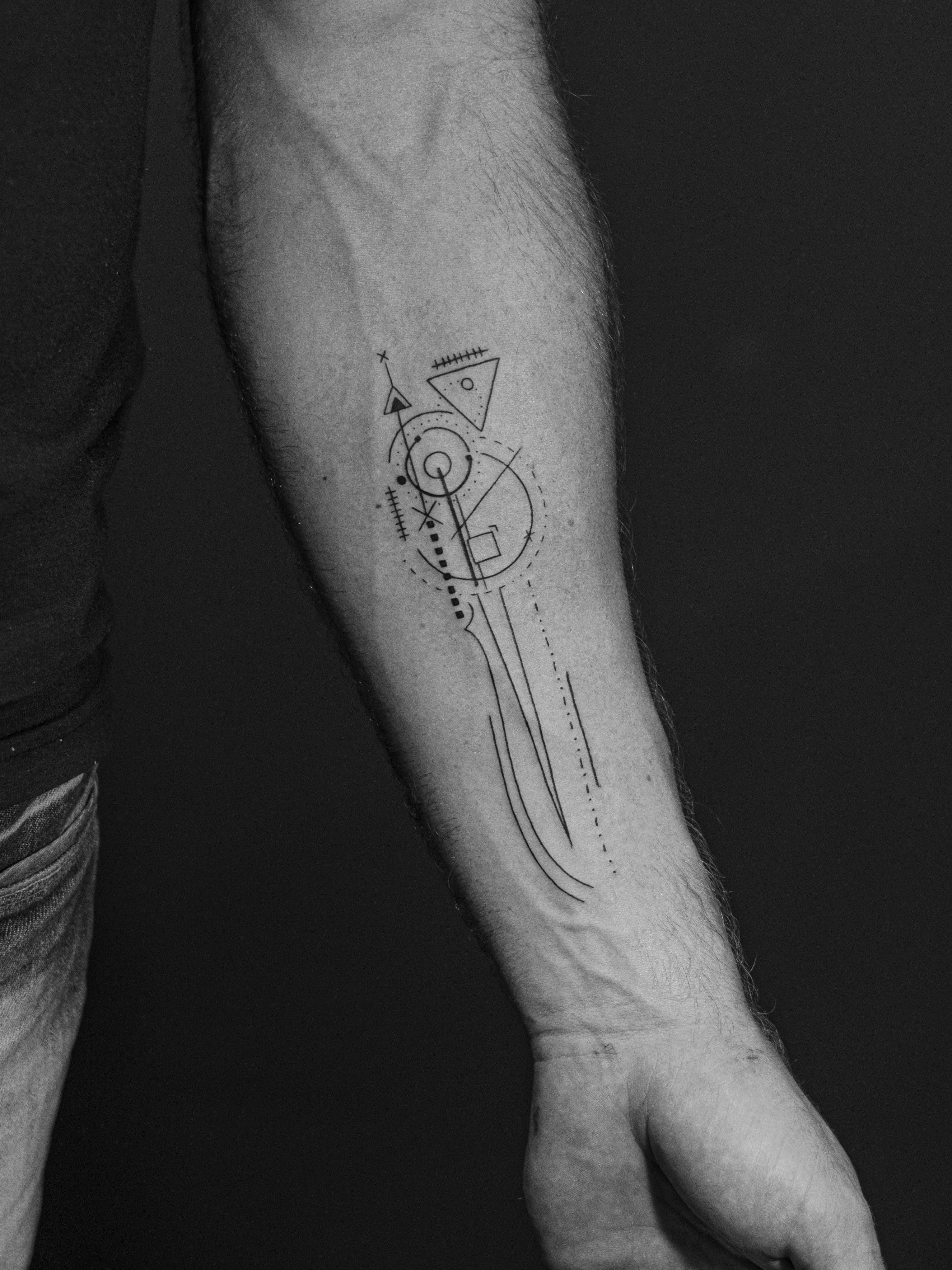 Tatuagem minimalista feita em linha fina (fineline) na região do antebraço, representando linhas abstratas.