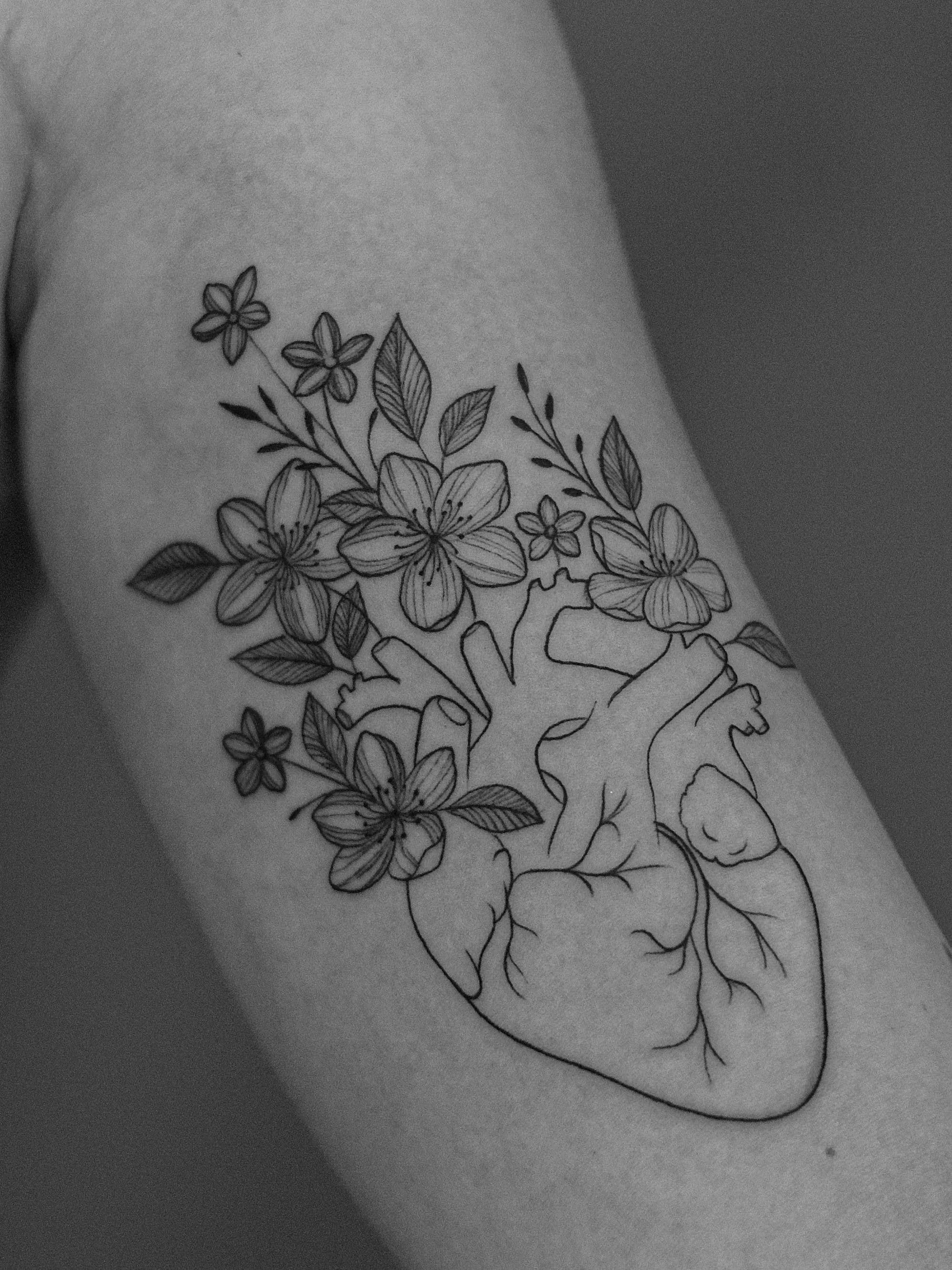 atuagem minimalista feita em linha fina (fineline) na região do biceps, representando um coração humanos, com flores saindo pelas veias e artérias do coração.