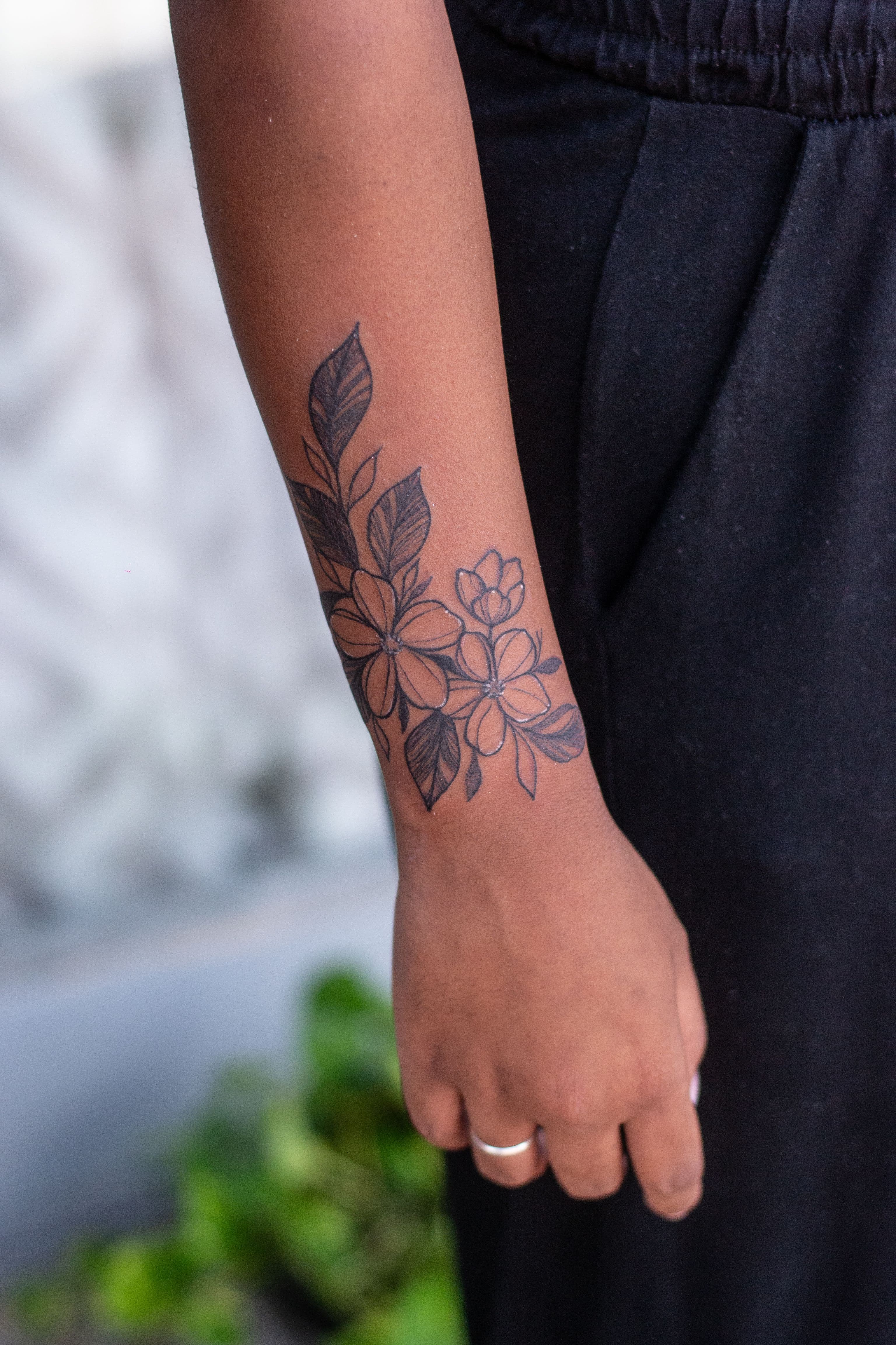 Tatuagem floral em liha fina no antebraço próxima ao pulso.