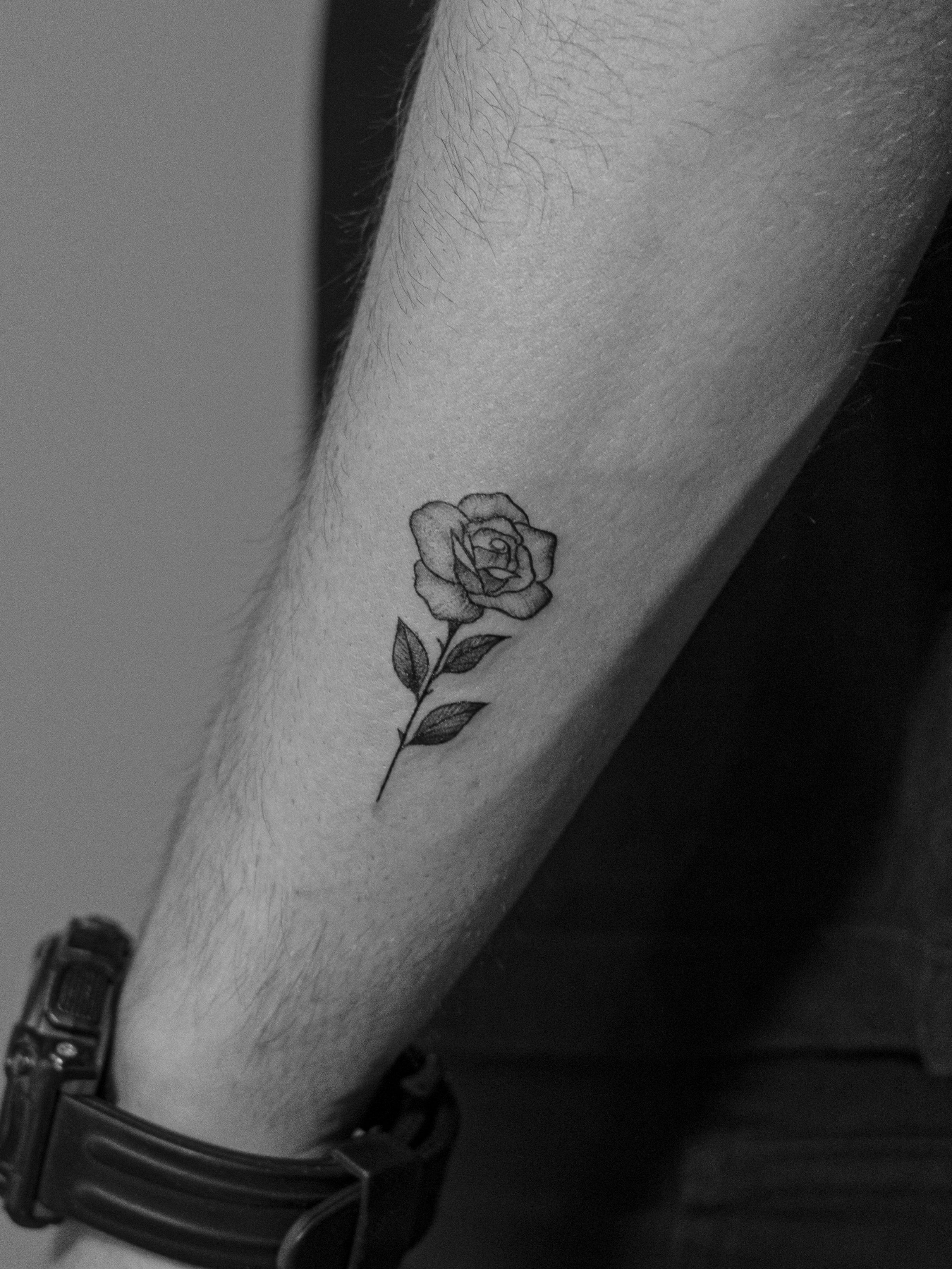 Tatuagem minimalista feita em linha fina (fineline) na região do antebraço, representando uma rosa (flor).