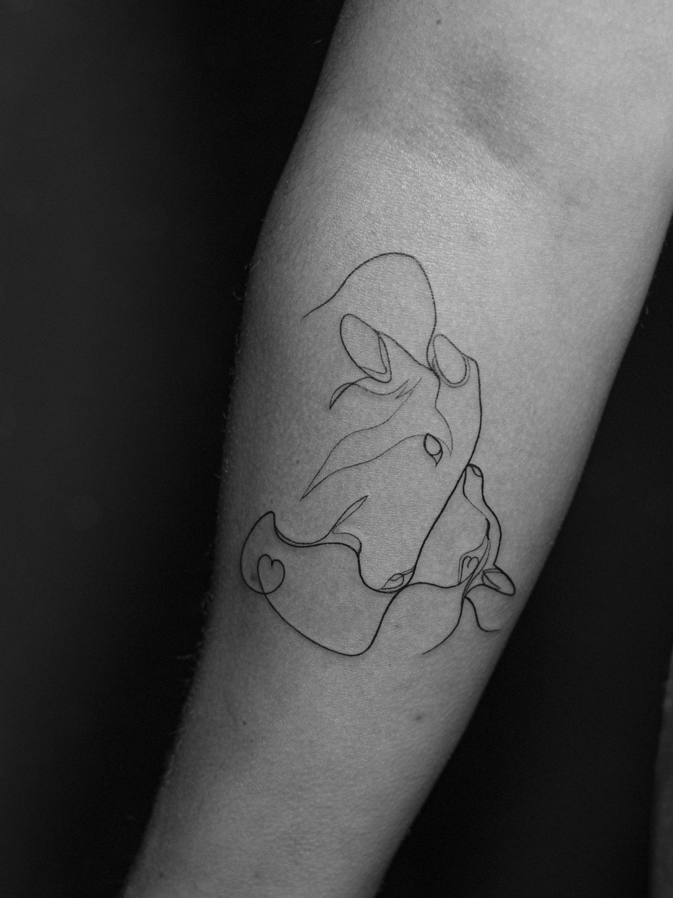 Tatuagem minimalista feita em linha fina (fineline), estilo linha contínua (oneline) na região do antebraço, representando uma vaca e seu filhote.
