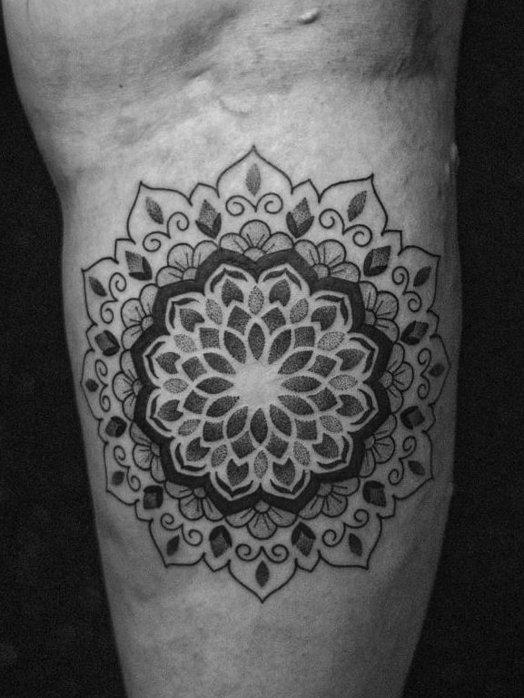 Tatuagem feita em pontilhismo (dotwork) e linha fina (fineline) na região da panturrilha, representando uma flor/mandala.