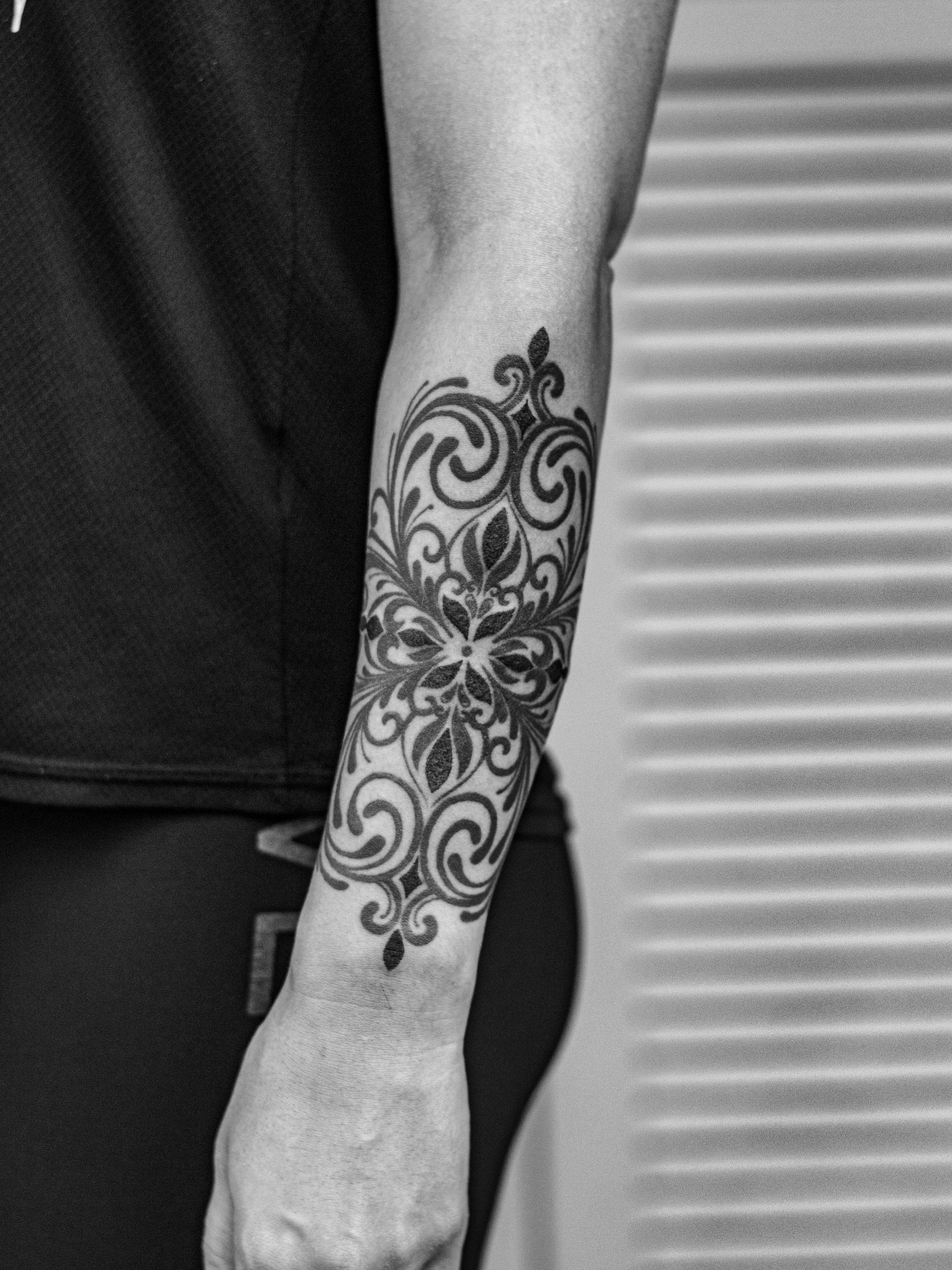 Tatuagem ornamental feita em pontilhimo (dotwork), somente em preto (blackwork), na região do antebraço, representando ornamentos e flores mandalas.